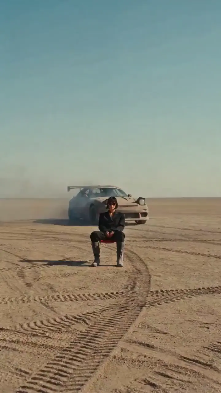 Woman seated in front of a sports car on a desert plain